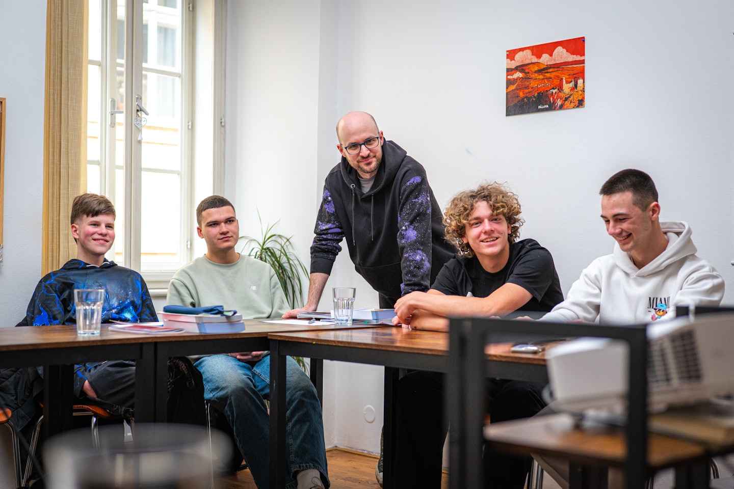 A teacher smiles while instructing four students around a table.